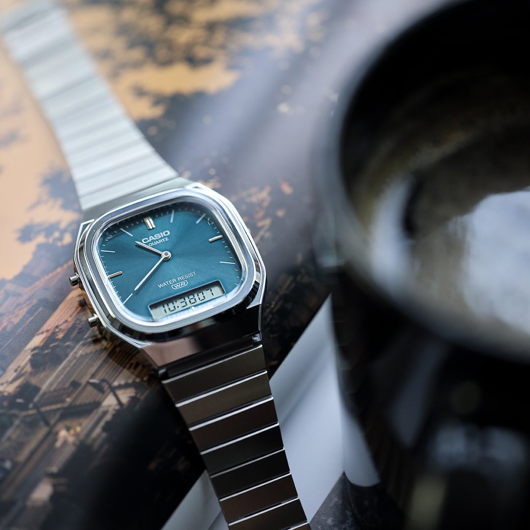 A blue casio watchon a magazine, a cup of coffee next to it