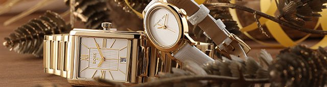 Two gold toned watches on a wood background with gold sprayed plants