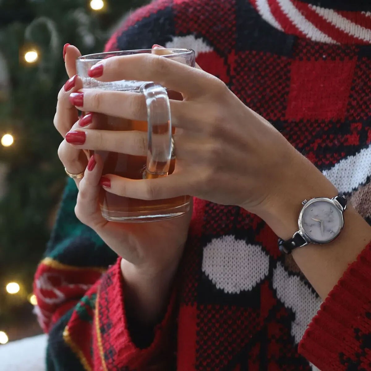 Frauenhände mit roten Fingernägeln halten eine Tasse Tee und tragen einen Weihnachtspullover