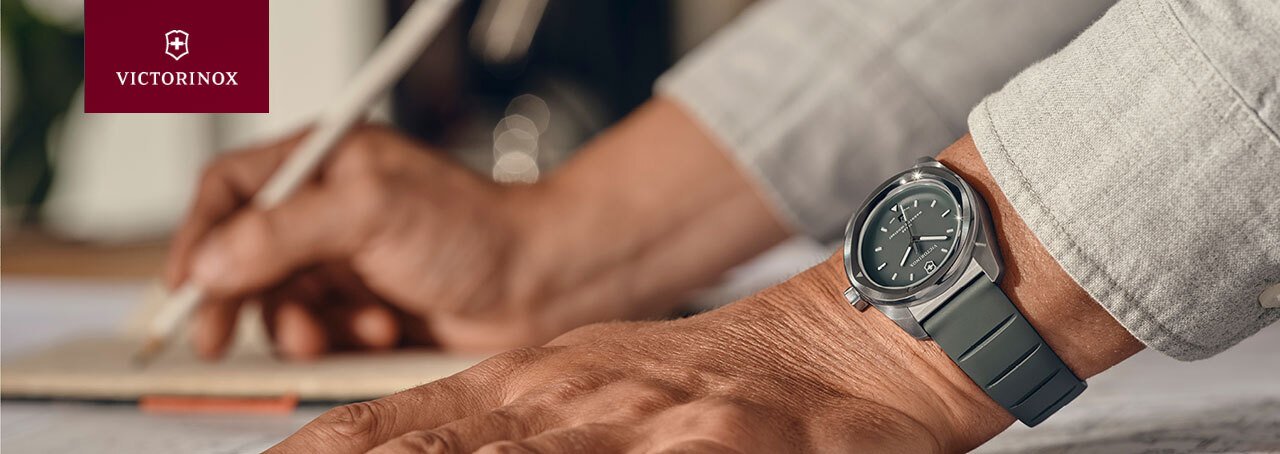 A man's hands leaning on a table with a Victorinox watch and logo
