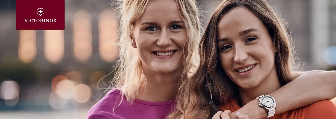 Twee lachende jonge vrouwen. De ene heeft haar arm om de schouder van de andere en toont haar Victorinox dameshorloge.